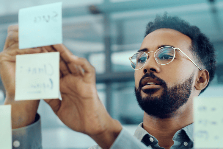 A young man setting goals and sticking notes on a glass wall